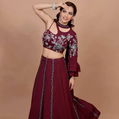 This maroon Indo-Western lehenga is all about modern style. The outfit features a unique one-shoulder blouse with a cutout detail and bell sleeve, paired with a flowing skirt. The blouse is adorned with beautiful floral embroidery.