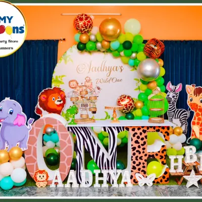 A full-stage jungle theme for a "Wild One" first birthday. This setup features character cutouts of a lion, elephant, zebra, and giraffe, large 'ONE' marquee letters with animal prints, and a lush green and gold balloon arch.
