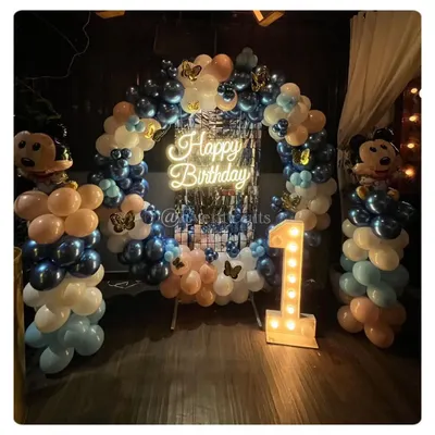 A Mickey Mouse themed birthday with a stylish twist. This circular balloon arch uses a cool palette of blue, white, and nude tones, with a 'Happy Birthday' neon sign and Mickey Mouse foil balloons.