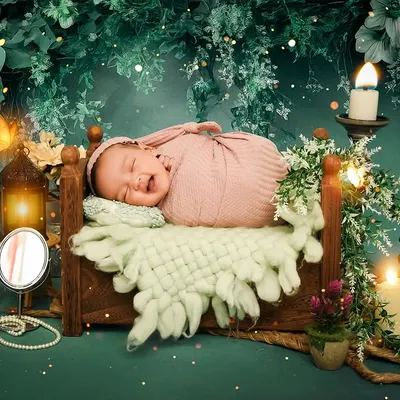 A baby smiles in their sleep while nestled in a tiny bed in an enchanted forest setup. The warm candlelight and magical sparkles create a truly dreamy atmosphere for this newborn portrait.