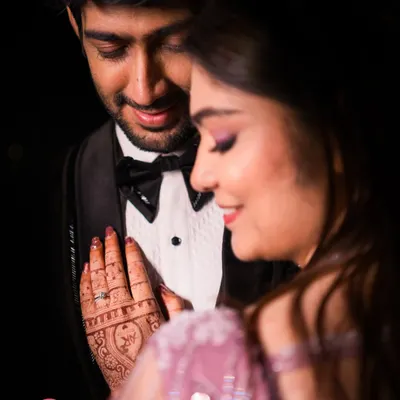 An intimate close-up under dramatic lighting. We focus on the details, from the henna on her hand to the adoration in his eyes.