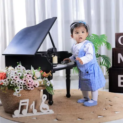 Celebrating her first birthday with a musical theme. This little girl looks adorable standing by our miniature grand piano, a perfect prop for a classic and elegant milestone photoshoot.