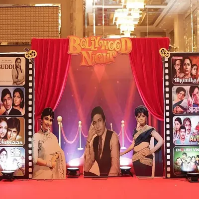 The main stage for a 60th birthday, designed with a 'Bollywood Night' retro theme. We used a red curtain backdrop, film reel props, and cutouts of classic movie stars.