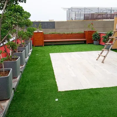 A rooftop garden design featuring a combination of artificial turf for a green lawn effect and a dedicated patio area. The space is lined with potted plants and includes a custom wooden bench with integrated planters.