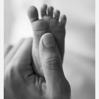A father's thumb gently holds his baby's entire foot. This timeless black and white image is a powerful illustration of how tiny they are in these first few days.