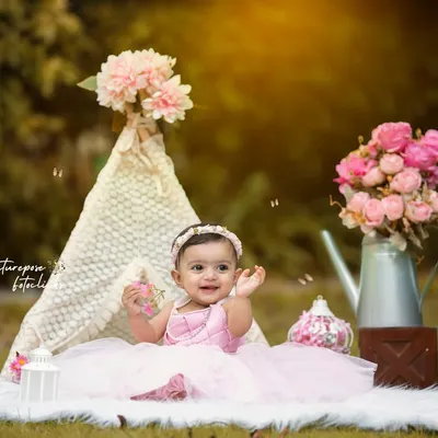 A whimsical outdoor portrait session with a boho-chic theme. This little girl is all smiles in a beautiful pink dress, surrounded by a lace teepee and floral props that create a magical, fairytale-like setting.