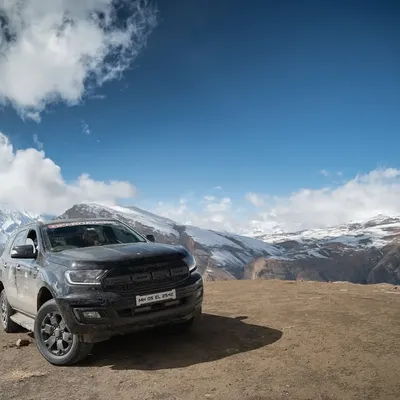 A rugged, all-black Ford Endeavour is parked on a dirt lookout, with the vast, snow-covered peaks of the Himalayas stretching out behind it. This shot emphasizes the vehicle's powerful presence in an extreme environment.