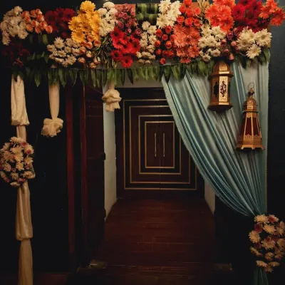 An entrance arch designed for an evening engagement. The decor features a thick arrangement of red, orange, and white flowers, with draped fabric and hanging Moroccan lanterns to create a warm and inviting entryway.