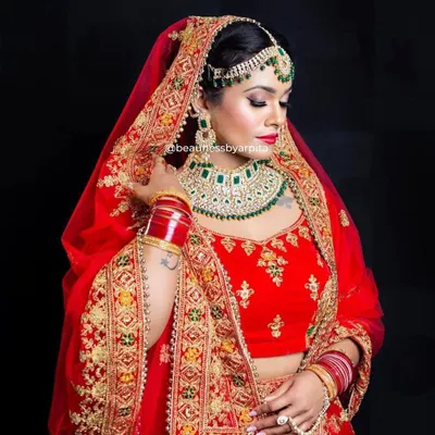 A classic red bridal lehenga with heavy gold embroidery and emerald green jewellery accents. This is a timeless look for the main wedding ceremony, ensuring you look nothing less than a queen.