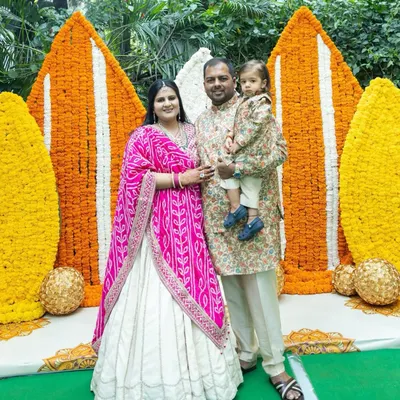 A beautiful family portrait from a Myra ceremony, set against a stunning backdrop of orange and white marigold panels. It's a perfect blend of tradition, celebration, and family love.