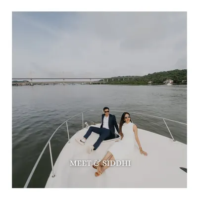 A wide-angle shot of the couple relaxing on the bow of a yacht in Goa. This image captures the feeling of freedom and luxury, with the expansive water and bridge in the background.