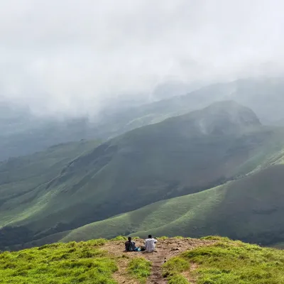Two trekkers finding a moment of peace, gazing out at the endless green valleys of Kudremukha. These are the views that make the climb worth every step.