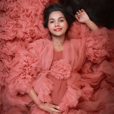 A signature artistic portrait featuring a mom-to-be lying down, completely surrounded by the ruffles of her dramatic pink gown.