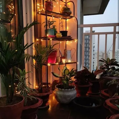 We used a simple metal corner shelf to create a multi-level plant display on this balcony. Wrapping the structure with warm fairy lights adds a cozy and magical glow to the green corner in the evening.