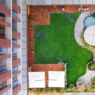 An aerial view of a residential terrace project, showcasing a thoughtful layout that combines lush artificial turf, wooden decking, and a curved stone pathway leading to a jacuzzi and gazebo area.