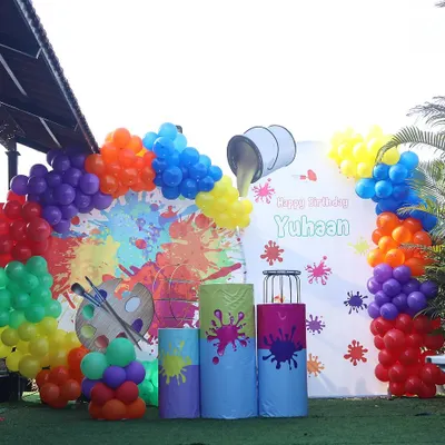 A vibrant and creative art-themed birthday party. This outdoor setup features a paint splatter backdrop and a rainbow of balloon colors, perfect for a budding artist.