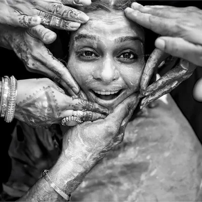 A powerful black and white shot from a Haldi ceremony. The hands of loved ones frame the bride's joyful face, creating a moment that is both intimate and full of energy.