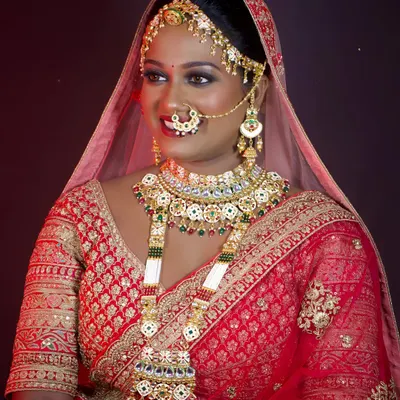 A radiant bride adorned in a magnificent, heavy bridal set featuring Kundan work and green stones. This entire set, from the matha patti to the long necklace, is available for rent.