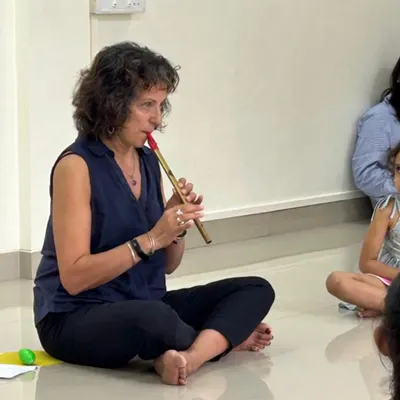 Naheed Shimala uses a simple wind instrument during a class. This demonstrates the use of varied instruments to introduce concepts of pitch, timbre, and breath control in an accessible way for young children.