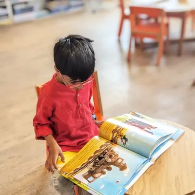 A young bookworm completely absorbed in a picture book. It's moments like these, of quiet focus and discovery, that we aim to create in our cozy reading spaces.