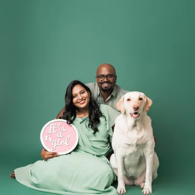 The perfect family announcement! This beautiful couple is joined by their proud Labrador, who is clearly excited to become a big sister. The "It's a girl!" sign adds a lovely touch to this studio maternity portrait.