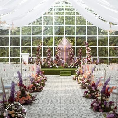 The aisle view of this stunning church-inspired wedding ceremony. The floral-lined path leads to a beautiful altar, all set against a glasshouse backdrop that brings the outdoors in.