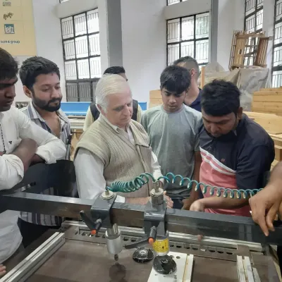 An instructor demonstrates the use of a multi-boring machine to a group of attentive students, a key piece of equipment for creating accurate holes for dowels and hardware.