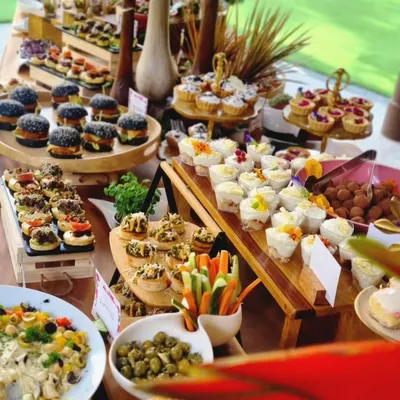 A vibrant and abundant grazing table, showcasing a mix of mini charcoal burgers, assorted canapés, fresh vegetables, and dessert cups. This spread is a perfect example of how we combine diverse flavors and textures for a complete culinary journey.