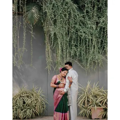 A full-length portrait of an expecting couple against a modern wall with hanging greenery. This image showcases how I blend contemporary backdrops with traditional maternity attire for a unique look.