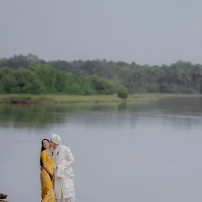 A groom-to-be gently kisses his partner's cheek as they stand by a calm, expansive river. This is a perfect example of a tender, romantic moment captured in a serene natural setting.