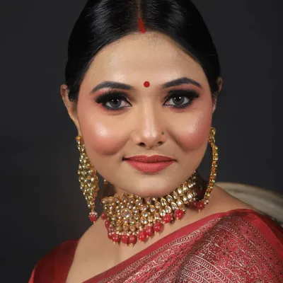 A classic and elegant party makeup look on a model in a red Banarasi saree. The makeup features a flawless base, sharp winged eyeliner, and a complementary red lip for a timeless finish.