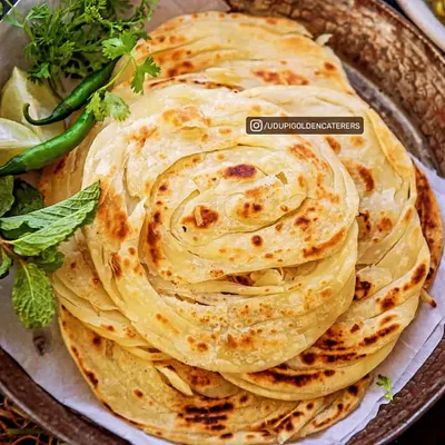 A stack of freshly made Kerala Parottas, showcasing their intricate, flaky layers. These are cooked live on a tawa, ensuring each guest experiences their soft, chewy, and crispy texture.