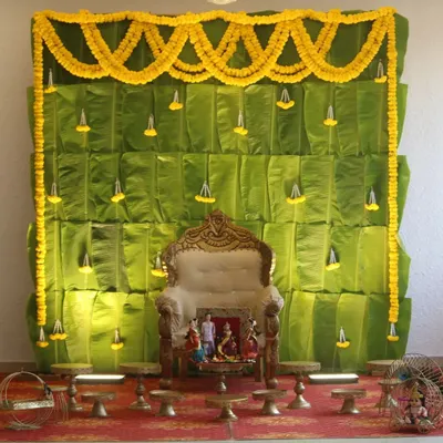 A traditional Seemantham decor featuring a backdrop made entirely of fresh banana leaves, adorned with marigold garlands.