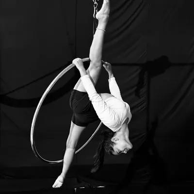 This stunning black and white photo captures an advanced student holding a perfect vertical split on the aerial hoop, showcasing incredible flexibility and control.