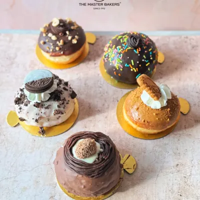 An assortment of our golden, fluffy Bomboloni, also known as filled donuts. This lineup includes flavors like Ferrero Rocher, Oreo, Lotus Biscoff, classic chocolate sprinkle, and hazelnut chocolate.