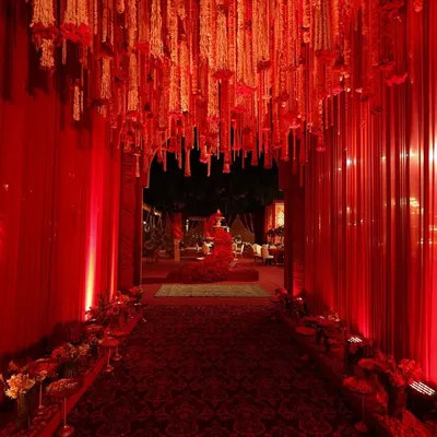 This grand crimson aisle, draped in flowing curtains and adorned with cascading floral chandeliers, was designed to create a regal and immersive welcome.