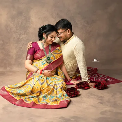 An intimate moment between a couple during their traditional maternity shoot. The rich colors of the saree and the warm studio lighting create a beautiful, classic portrait.