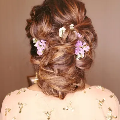 A detailed shot of this stunning party hairstyle. This intricate, messy bun is woven with delicate purple and white flowers, making it perfect for a sangeet or reception guest.
