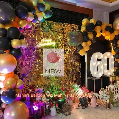 A chic and modern 60th-anniversary celebration. The decor features a dazzling gold and silver shimmer wall, a black and gold balloon arch, and large marquee numbers.