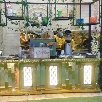My elegant live coffee bar setup, decorated with green vines. The station is equipped with a coffee machine, grinder, and various syrups for a complete café experience.