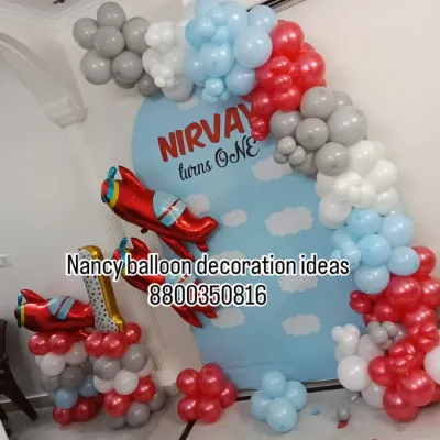 An airplane-themed first birthday decoration for Nirvay. I used a custom-printed backdrop with clouds and created a balloon arch in red, grey, and light blue, adding airplane foil balloons to complete the theme.