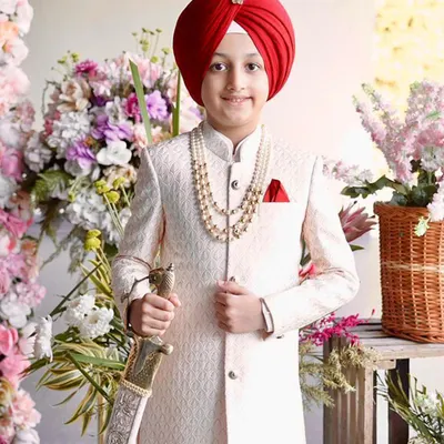 This little star is ready for his big moment in a stunning off-white sherwani, complete with a pearl necklace and a royal red turban. It is a timeless look, tailored for unforgettable wedding celebrations.