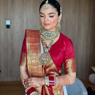A beautiful South Indian bride, Aishwarya, in a traditional red and white silk saree. The makeup is classic and radiant, with a focus on clean skin.