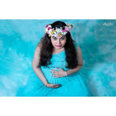 An artistic studio portrait taken from a high angle. The mother-to-be, seated in a sea of blue fabric, looks up at the camera, creating a dramatic and captivating image.