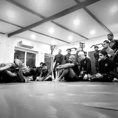 A black and white shot of a group learning the fine points of a Jiu-Jitsu technique. In this sport, inches and details matter more than anything. We teach you to focus on the fundamentals.