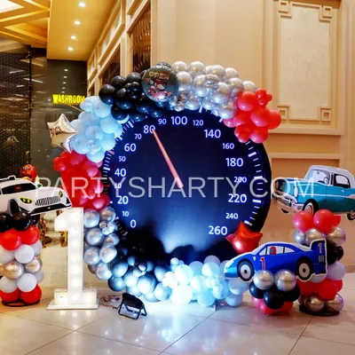 A creative photo opportunity for a car-themed party, featuring a giant speedometer backdrop and car-shaped balloon sculptures.