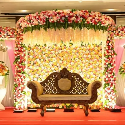 A magnificent floral stage we created for a wedding reception. This design features a dense wall of pink, white, and yellow flowers with hanging floral strings, creating a truly grand backdrop.