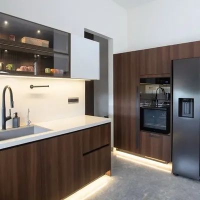 This angle highlights the seamless integration of appliances. The built-in oven and side-by-side refrigerator are flush with the walnut cabinetry, creating an uncluttered wall of storage that is both beautiful and highly functional.