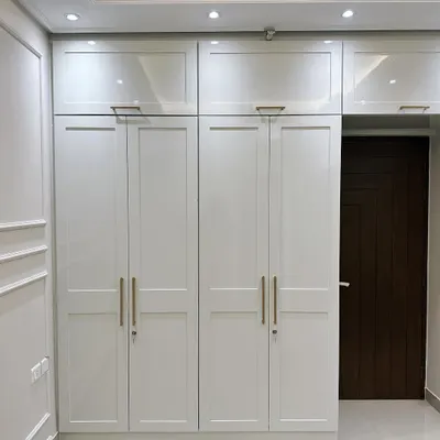 A floor-to-ceiling white wardrobe designed in a modern Victorian style. This piece features classic panelled doors with sleek golden handles and provides ample overhead storage, blending timeless design with practical functionality.