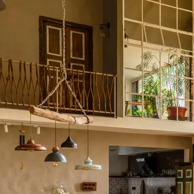 This double-height living space in The Brick Loft features exposed brick, large windows, and a unique railing made from jute. The hanging light fixture is crafted from an upcycled wooden log.
